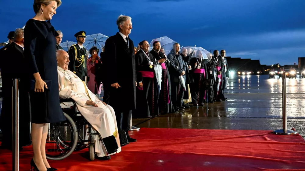 Pope Francis, flanked by Belgian King Philippe and Queen Mathilde, reacts after arriving at Melsbroek Military Air Base for a four-day apostolic journey, in Steenokkerzeel, Belgium, September 26, 2024. Vatican Media/­Handout via REUTERS  ATTENTION EDITORS - THIS IMAGE WAS PROVIDED BY A THIRD PARTY.