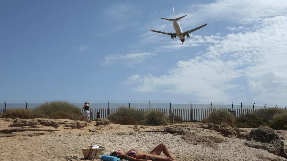 ﻿A woman sunbathes on the beach as an airplane lands at the Balearic Islands capital of Palma de Mallorca, Spain, Wednesday, July 29, 2020. Concerns over a new wave of coronavirus infections brought on by returning vacationers are wreaking havoc across Spain's tourism industry, particularly in the Balearic Islands following Britain's effective ban on travel to the country. (AP Photo/Joan Mateu