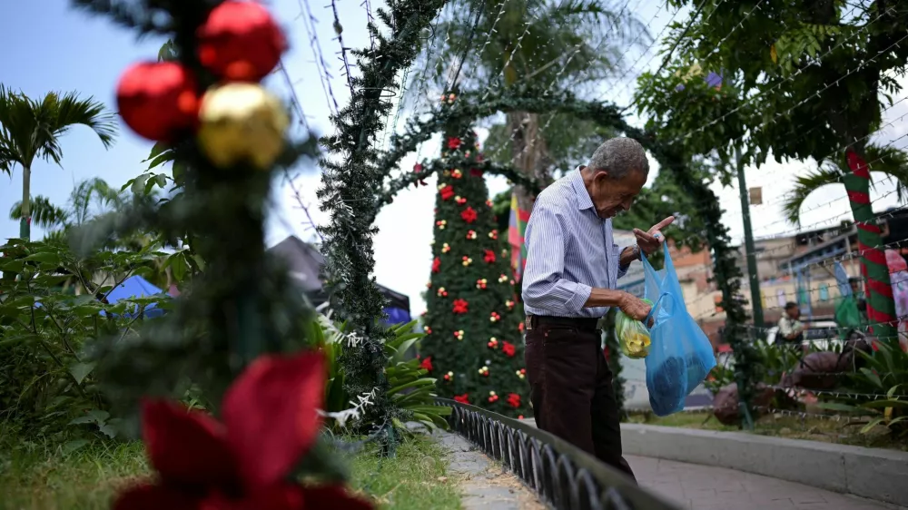 A man checks a plastic bag with food in front of Christmas decorations at a public square, as the Christmas season kicks off as per a decree of Venezuela's President Nicolas Maduro, in Caracas, Venezuela October 1, 2024. REUTERS/Gaby Oraa   TPX IMAGES OF THE DAY