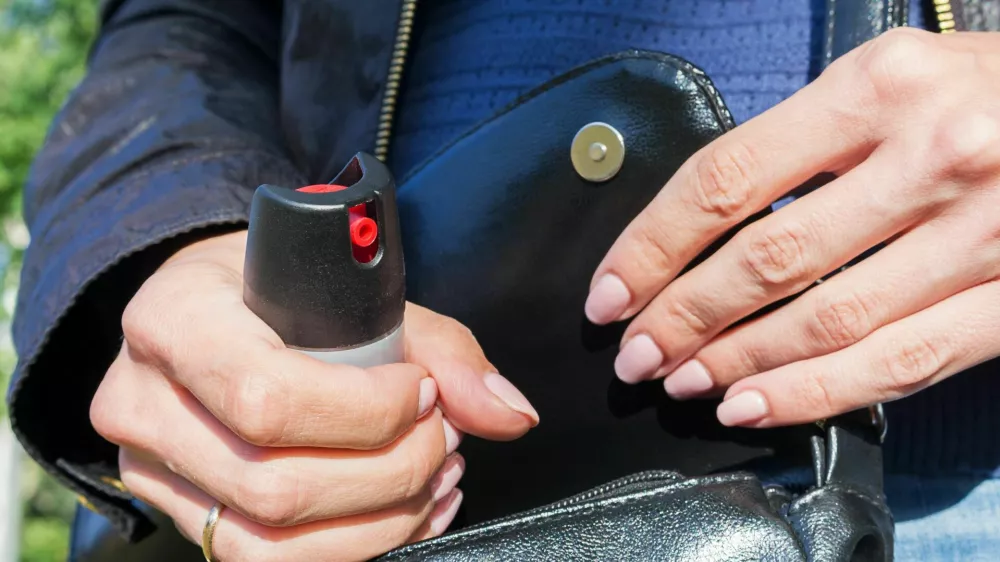 A young woman pulls a can of tear gas or bottle of pepper spray out of her purse. Means of self-defense, protection from robbery and rape.. Selective focus, close-up. / Foto: Evgen_prozhyrko