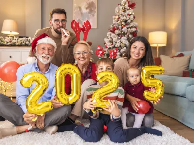 Beautiful happy family celebrating Christmas at home, having fun holding giant balloons shaped as numbers 2025, representing the upcoming New Year / Foto: Vladans