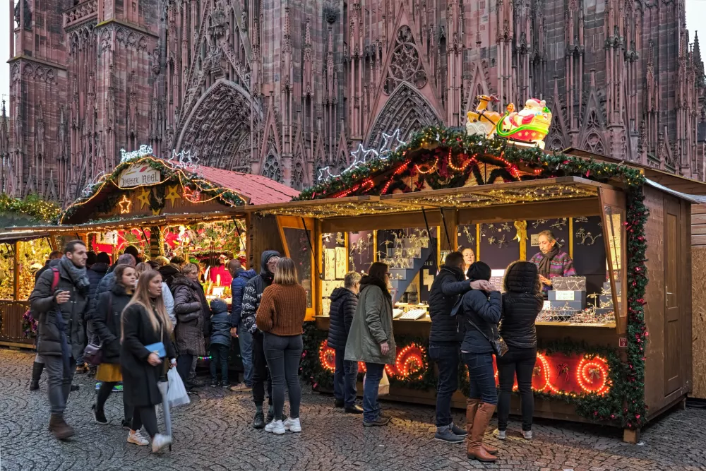 Strasbourg, France - December 15, 2019: Market stalls with Christmas presents at Christmas market in front of Strasbourg Cathedral. Unknown people walk along the market stalls. Strasbourg has been holding Christmas market around its cathedral since 1570, making it one of the oldest Christmas markets in Europe.