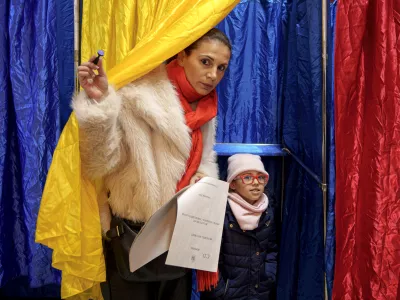 A woman and child exit a voting cabin with the colours of the Romanian flag as curtains, during the country's parliamentary elections, in Bucharest, Romania, Sunday, Dec. 1, 2024. (AP Photo/Andreea Alexandru)