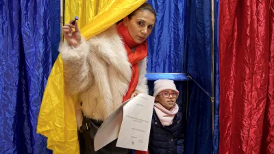 A woman and child exit a voting cabin with the colours of the Romanian flag as curtains, during the country's parliamentary elections, in Bucharest, Romania, Sunday, Dec. 1, 2024. (AP Photo/Andreea Alexandru)