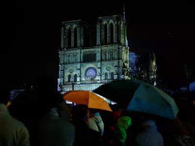 People protect themselves from the rain under umbrellas as they watch on a screen the reopening service ceremony of the Notre-Dame de Paris Cathedral, five-and-a-half years after a fire ravaged the Gothic masterpiece, as part ceremonies to mark the Cathedral's reopening after its restoration, in Paris, France, December 7, 2024. REUTERS/Sarah Meyssonnier