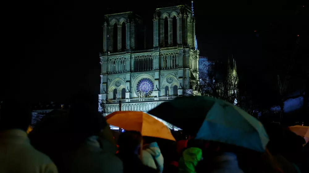 People protect themselves from the rain under umbrellas as they watch on a screen the reopening service ceremony of the Notre-Dame de Paris Cathedral, five-and-a-half years after a fire ravaged the Gothic masterpiece, as part ceremonies to mark the Cathedral's reopening after its restoration, in Paris, France, December 7, 2024. REUTERS/Sarah Meyssonnier