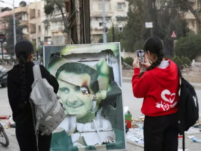 Women use their mobile phones near a damaged picture of Syrian President Bashar al-Assad as people celebrate, after Syrian rebels announced that they have ousted President Bashar al-Assad, in Qamishli, Syria December 8, 2024. REUTERS/Orhan Qereman