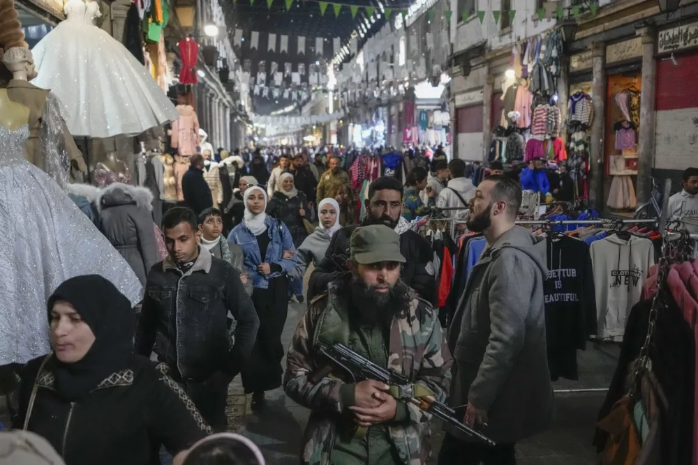 An armed opposition fighter walks among costumers at the Al-Hamidiyeh market inside the old walled city of Damascus, Syria, Tuesday, Dec. 10, 2024. (AP Photo/Hussein Malla)