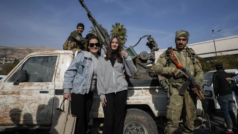 Syrian women pose for a photograph as they stand next to opposition fighters in Damascus, Syria, Tuesday, Dec. 10, 2024. (AP Photo/Omar Sanadiki)