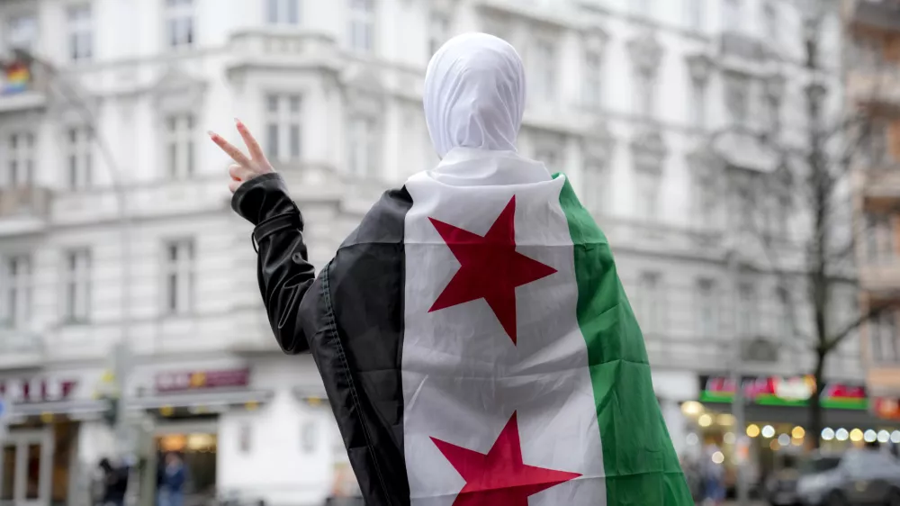 A Syrian girl flashes victory sign in a street in Berlin while wearing a Syrian opposition flag, Tuesday, Dec. 10, 2024. (AP Photo/Ebrahim Noroozi)