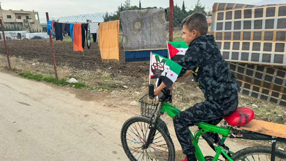 A boy rides a bike decorated with flags with Syrian opposition colours in an informal tented settlement in Bar Elias, in the Bekaa Valley, Lebanon December 11, 2024. REUTERS/Ali Hankir