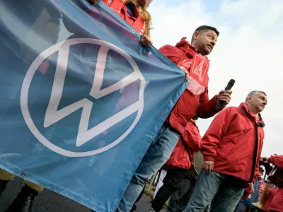 FILE PHOTO: A man wearing an IG Metall (Industrial Union of Metalworkers) scarf holds a banner with the Volkswagen logo, as workers gather to strike against planned cuts to wages and possible factory closures, in Hanover, Germany, December 2, 2024. Picture taken with long exposure. REUTERS/Fabian Bimmer/File Photo