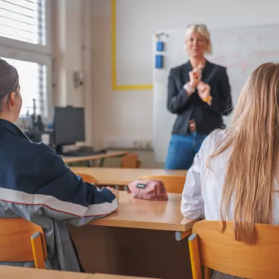 Rear view of two female students during a lecture in the classroom, looking at female teacher teaching and writing on a blackboard / Foto: 24k-production