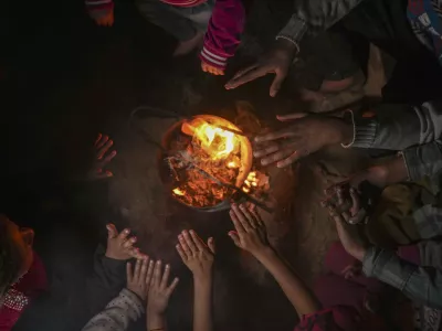 Reda Abu Zarada, 50, displaced from Jabaliya in northern Gaza, warms up by a fire with her grandchildren at a camp in Khan Younis, Gaza Strip, Thursday, Dec. 19, 2024. (AP Photo/Abdel Kareem Hana)