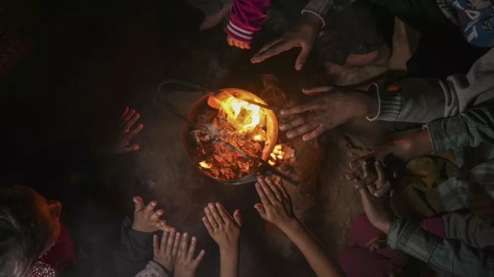 Reda Abu Zarada, 50, displaced from Jabaliya in northern Gaza, warms up by a fire with her grandchildren at a camp in Khan Younis, Gaza Strip, Thursday, Dec. 19, 2024. (AP Photo/Abdel Kareem Hana)