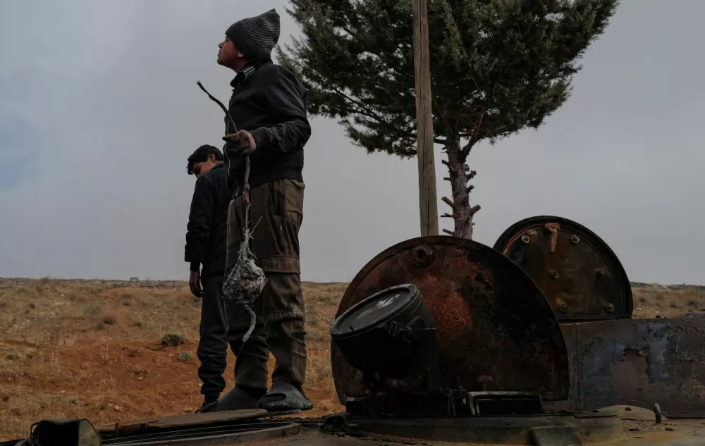 Ahmed and Khaled stand on an abandoned Syrian army armoured personnel carrier (APC) from which they collect metal to sell, outside Sednaya prison, which was known as a slaughterhouse under the rule of Syria's Bashar al-Assad, who was ousted, in Sednaya, Syria December 24, 2024. REUTERS/Zohra Bensemra