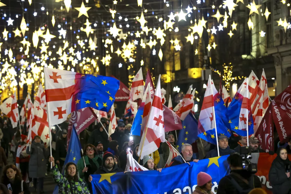 Demonstrators with Georgian national and EU flags march during an anti-government rally outside the Parliament building in Tbilisi, Georgia, on Saturday, Dec. 28, 2024. (AP Photo/Zurab Tsertsvadze)