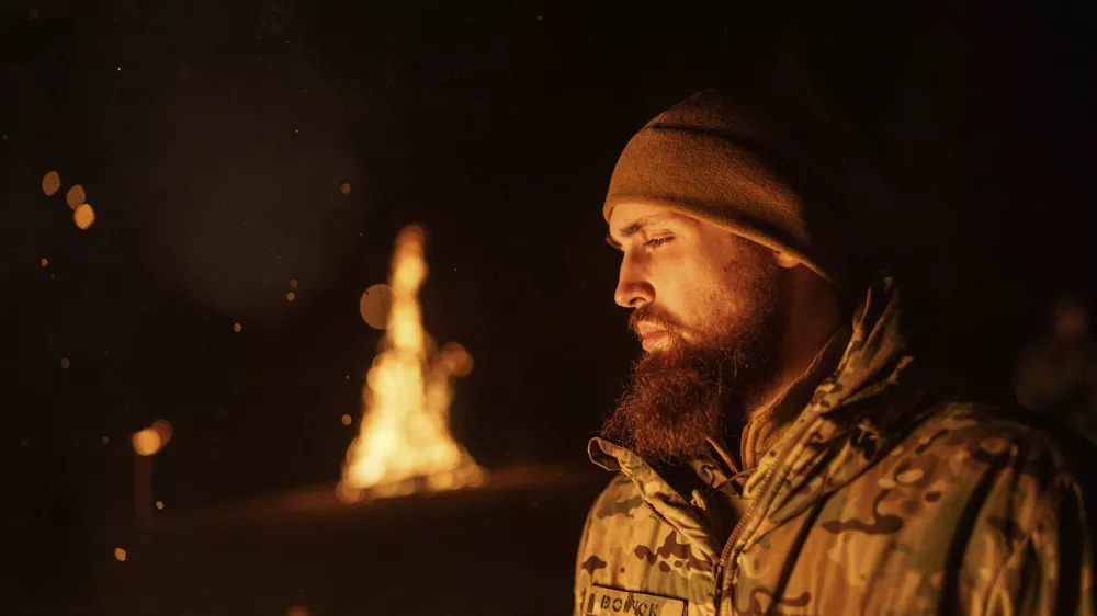 A Ukrainian serviceman aka Vovchok of 3rd assault brigade throws gunpowder into a fire during memorial ceremony of his fallen comrades during the winter solstice in Kharkiv region, Ukraine, Dec. 22, 2024. (AP Photo/Evgeniy Maloletka)