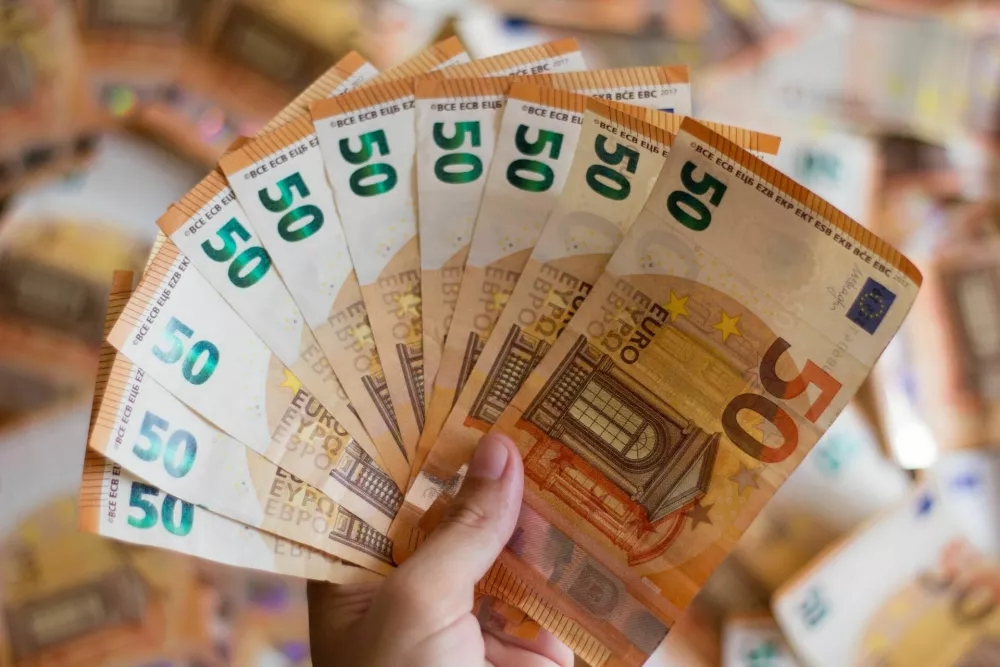 Picture of woman hand holding a lot of 50-euro notes with piles of bills in the background / Foto: Cristina Moliner