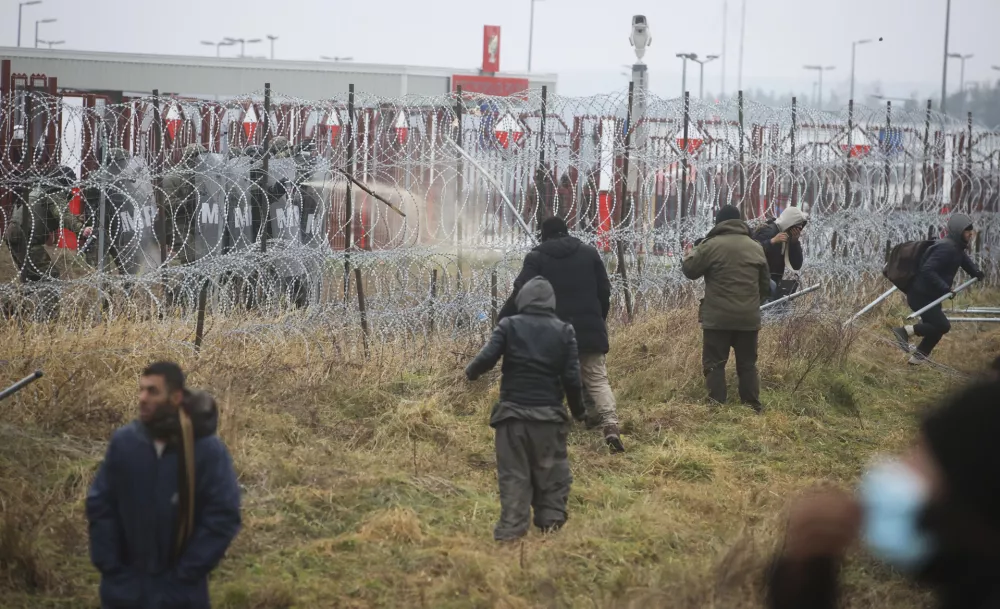 ﻿Polish servicemen, top left, spray tear gas during clashes between migrants and Polish border guards at the Belarus-Poland border near Grodno, Belarus, on Tuesday, Nov. 16, 2021. Polish border forces say they were attacked with stones by migrants at the border with Belarus and responded with a water cannon. The Border Guard agency posted video on Twitter showing the water cannon being directed across the border at a group of migrants in a makeshift camp. (Leonid Shcheglov/BelTA via AP)