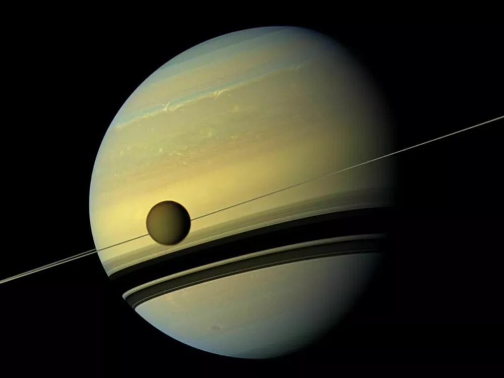 Saturn in njegova luna Titan. Tanka črta so Saturnovi prstani, gledani s strani, ki mečejo senco na planet. / Vir: Nasa/jpl-caltech/space Science Institute