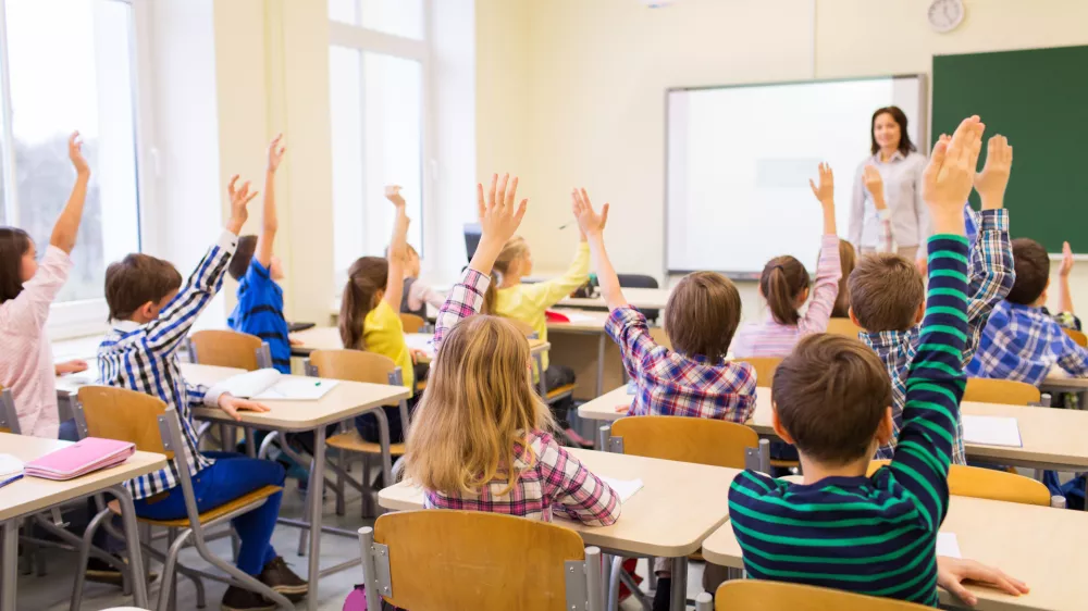 education, elementary school, learning and people concept - group of school kids with teacher sitting in classroom and raising hands