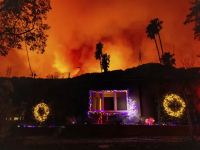 A helicopter drops water on the Palisades Fire behind a home with Christmas lights in Mandeville Canyon, Friday, Jan. 10, 2025, in Los Angeles. (AP Photo/Ethan Swope)