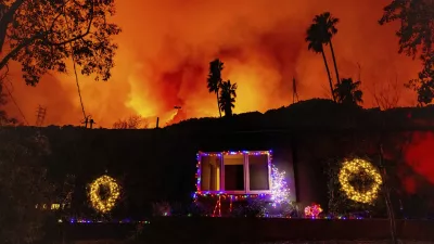 A helicopter drops water on the Palisades Fire behind a home with Christmas lights in Mandeville Canyon, Friday, Jan. 10, 2025, in Los Angeles. (AP Photo/Ethan Swope)