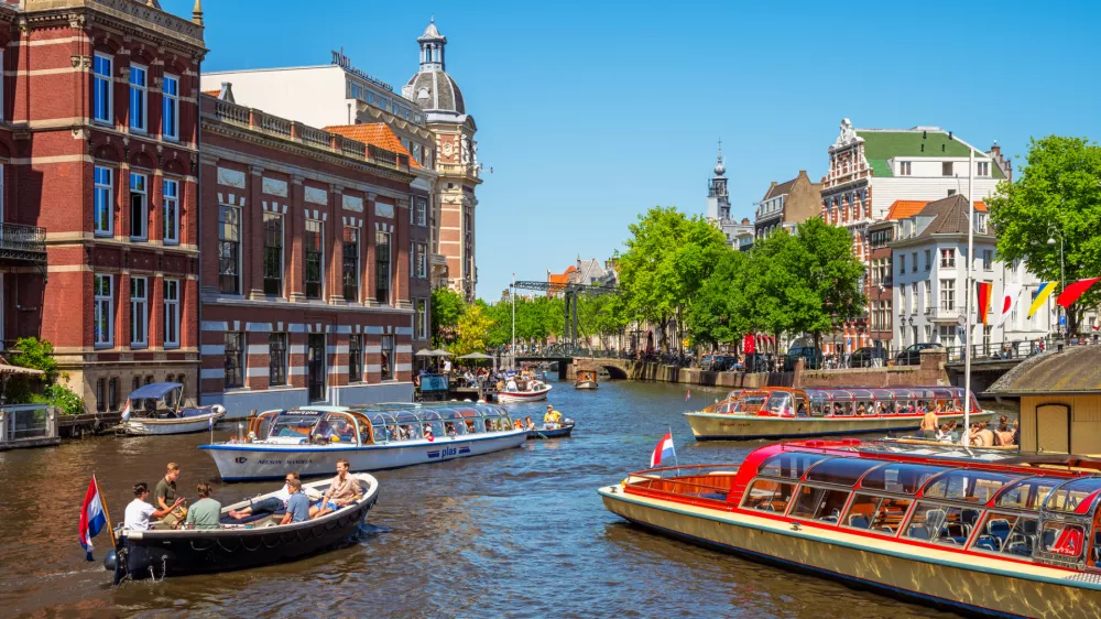 Amsterdam, Netherlands - June 3, 2023: Canal in Amsterdam, Netherlands busy with boat traffic on sunny saturday afternoon in June.