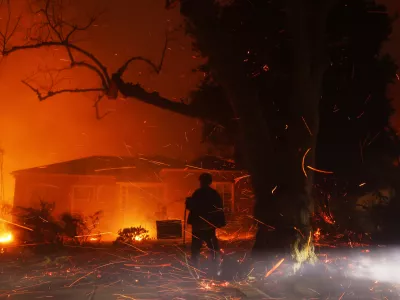 FILE - A person tries to hose down embers from the Palisades Fire in the Pacific Palisades neighborhood of Los Angeles, Jan. 7, 2025. (AP Photo/Etienne Laurent, File)