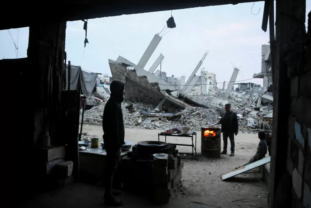 A Palestinian man looks on as another man cooks, near the rubble of buildings destroyed in previous Israeli strikes, ahead of a ceasefire set to take effect on Sunday, in Gaza City January 16, 2025. REUTERS/Hatem Khaled    TPX IMAGES OF THE DAY