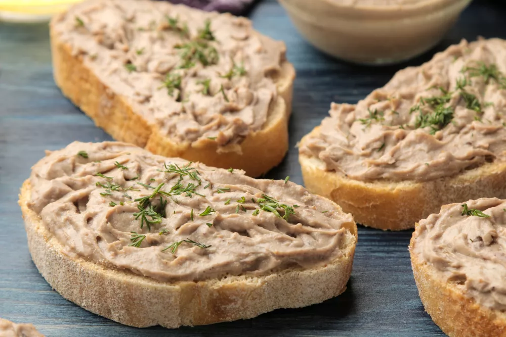 Fresh homemade chicken liver pate with herbs on bread on a blue wooden table. A sandwich. close-up / Foto: Kristina Maksymova