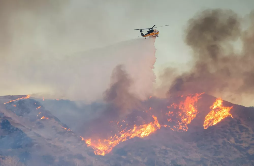 A helicopter drops water as the Hughes Fire burns in Castaic Lake, California, U.S. January 22, 2025. REUTERS/David Swanson