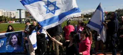 A woman waves an Israeli flag as people wait for the expected arrival of released Israeli hostages, who have been held in Gaza since the deadly October 7, 2023 attack by Hamas, as part of a prisoner-hostage exchange deal between Israel and Hamas, in Petah Tikva, Israel, January 25, 2025. REUTERS/Ronen Zvulun