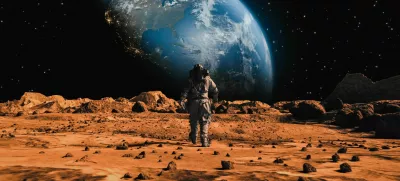 Following Shot of Brave Astronaut in Space Suit Confidently Walking on Mars Towards Earth Planet. Earth Planet as viewed from Mars surface. The surface of Mars, strewn with small rocks and red sand. Martian landscape in rusty orange shades, Mars Planet surface, Desert, Cliffs, sand. Red planet mars. Alien Red Planet Covered in Rocks. First Astronaut On the Mars. Big Moment for the Human Race. Advanced Technologies, Space Exploration/ Travel, Colonization Concept. / Foto: Nzoka John