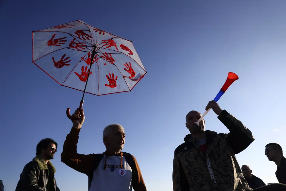 A man holds up an umbrella with painted red hands, a symbol representing the government's bloody hands, during a protest over the collapse of a concrete canopy that killed 15 people more than two months ago, in Novi Sad, Serbia, Saturday, Feb. 1, 2025. (AP Photo/Armin Durgut)