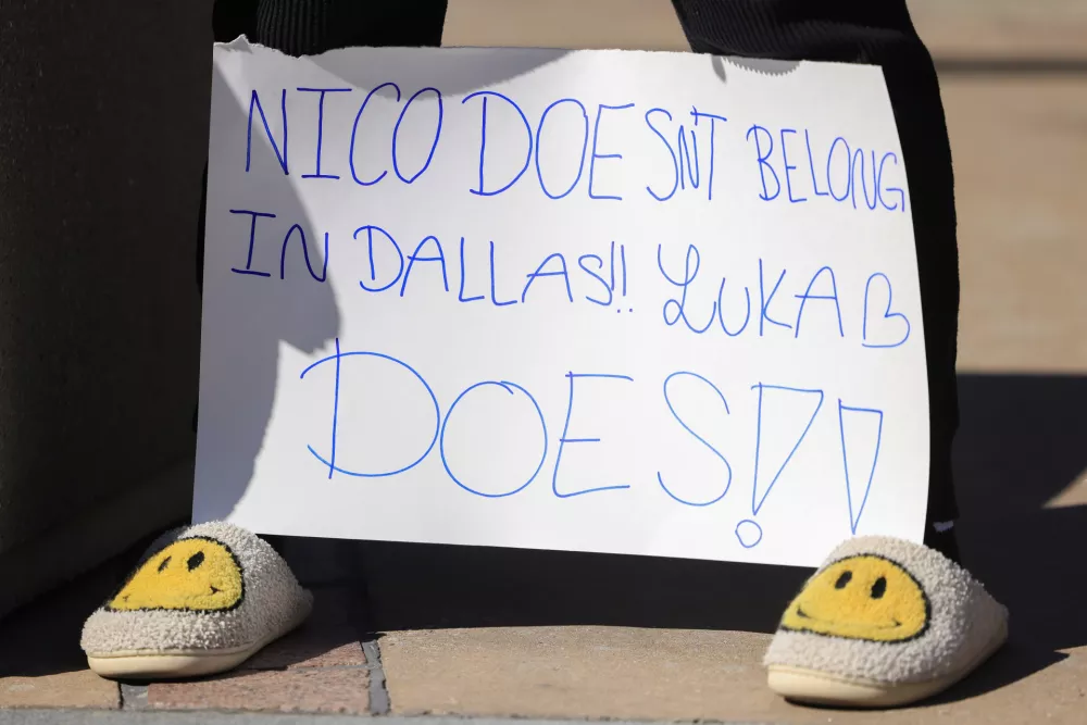 A woman holds a sign outside the American Airlines Center, Sunday, Feb. 2, 2025, in Dallas., Texas. (Elias Valverde II/The Dallas Morning News via AP)