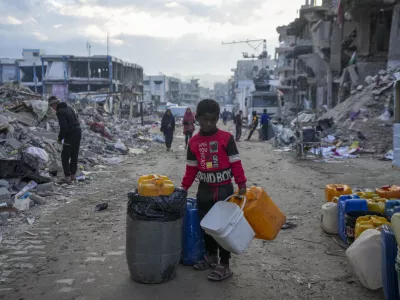 A young Palestinian kid carries jerricans along the destruction caused by the Israeli air and ground offensive in Jabaliya, Gaza Strip, Wednesday, Feb. 5, 2025. (AP Photo/Abdel Kareem Hana)