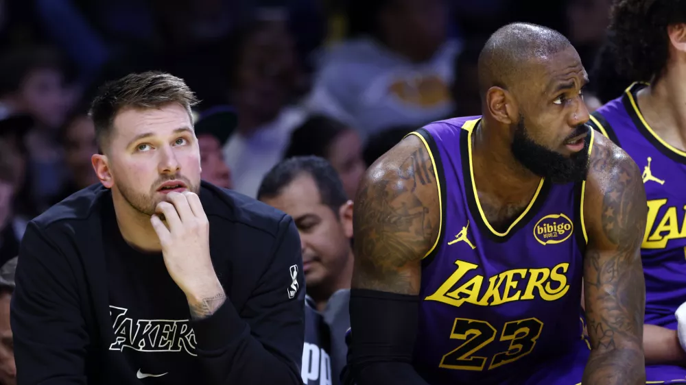 Los Angeles Lakers guard Luka Doncic, left, and forward LeBron James (23) look on from the bench during the first half of an NBA basketball game against the Golden State Warriors, Thursday, Feb. 6, 2025, in Los Angeles. (AP Photo/Kevork Djansezian)