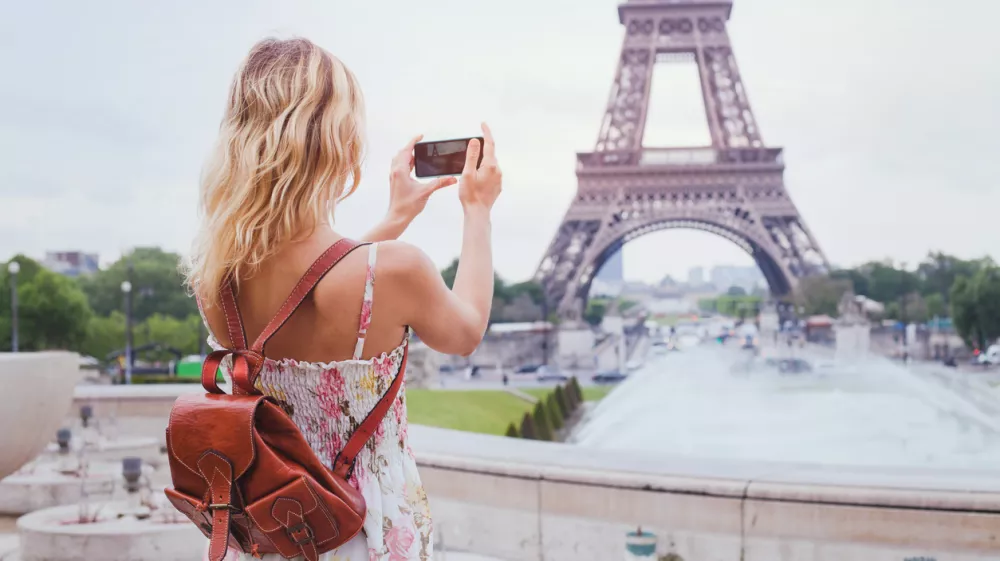 tourist taking photo of Eiffel tower in Paris with compact camera or smartphone, travel in Europe