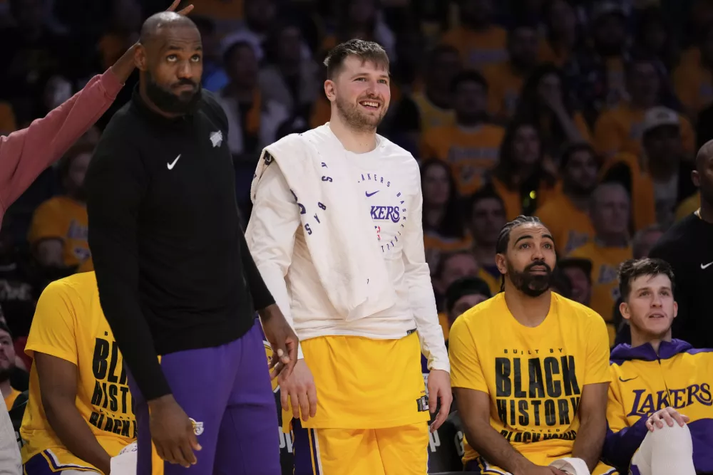 Los Angeles Lakers guard Luka Doncic, center, and teammate forward LeBron James, left, look on from the bench during the second half of an NBA basketball game against the Utah Jazz, Monday, Feb. 10, 2025, in Los Angeles. (AP Photo/Mark J. Terrill)