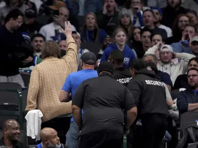 A pair of fans, one waving, are escorted out of the game after holding up a sign that said "Fire Nico," referencing the Dallas Mavericks general manager Nico Harrison in the second half of an NBA basketball game against the Sacramento Kings in Dallas, Monday, Feb. 10, 2025. (AP Photo/Tony Gutierrez)