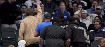 A pair of fans, one waving, are escorted out of the game after holding up a sign that said "Fire Nico," referencing the Dallas Mavericks general manager Nico Harrison in the second half of an NBA basketball game against the Sacramento Kings in Dallas, Monday, Feb. 10, 2025. (AP Photo/Tony Gutierrez)