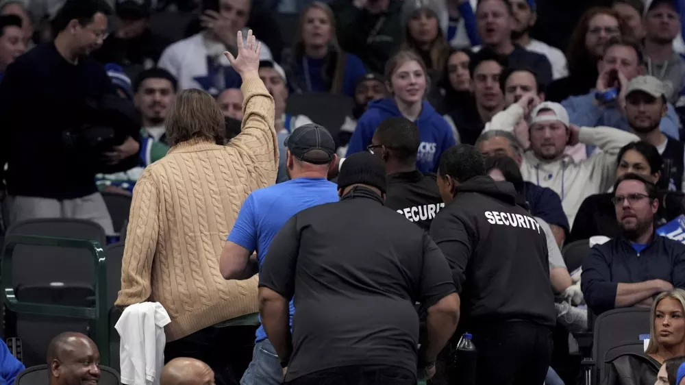 A pair of fans, one waving, are escorted out of the game after holding up a sign that said "Fire Nico," referencing the Dallas Mavericks general manager Nico Harrison in the second half of an NBA basketball game against the Sacramento Kings in Dallas, Monday, Feb. 10, 2025. (AP Photo/Tony Gutierrez)