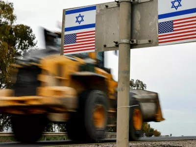 A construction vehicle drives past a sign with stickers depicting Israeli and U.S. flags, amid a ceasefire between Israel and Hamas, near kibbutz Mefalsim, Israel, February 11, 2025. REUTERS/Amir Cohen