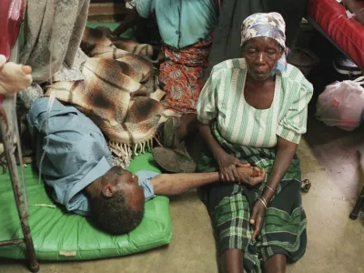 FILE - A woman holds the hand of a sick relative lying on the floor of the overcrowded Lilongwe Central Hospital, in Lilongwe, Malawi, Sept. 30, 1998, as the hospital is overflowing because of an epidemic of AIDS rampaging in southern Africa. (AP Photo /Denis Farrell, File)