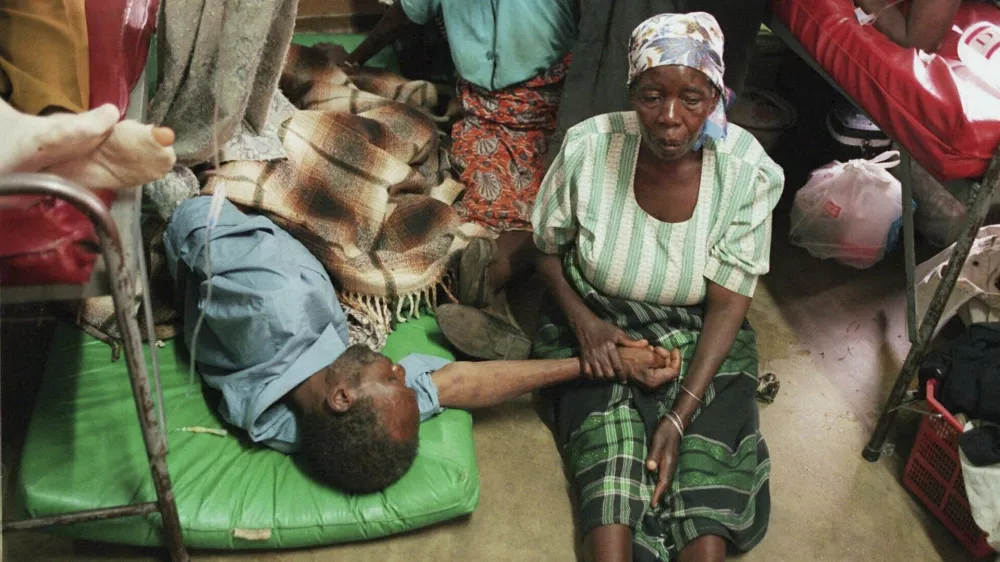 FILE - A woman holds the hand of a sick relative lying on the floor of the overcrowded Lilongwe Central Hospital, in Lilongwe, Malawi, Sept. 30, 1998, as the hospital is overflowing because of an epidemic of AIDS rampaging in southern Africa. (AP Photo /Denis Farrell, File)