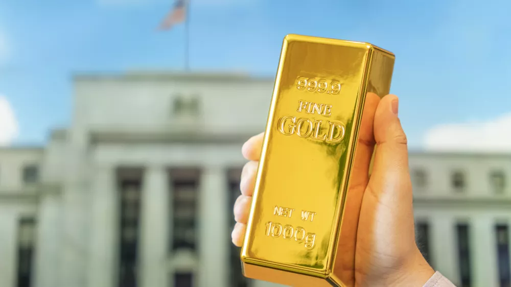 a gold bar in a man's hand against the background of the central bank, US Federal Reserve system. / Foto: Diy13