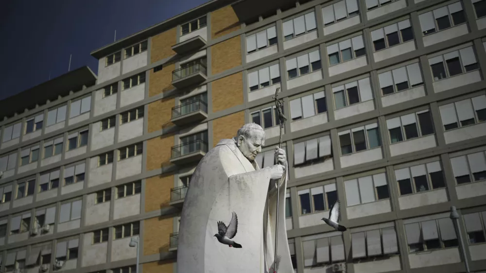 A marble statue of late Pope John Paul II is backdropped by the Agostino Gemelli Polyclinic in Rome, Saturday, Feb. 15, 2025, where Pope Francis was hospitalised Friday after a weeklong bout of bronchitis worsened and is receiving drug therapy for a respiratory tract infection. (AP Photo/Alessandra Tarantino)