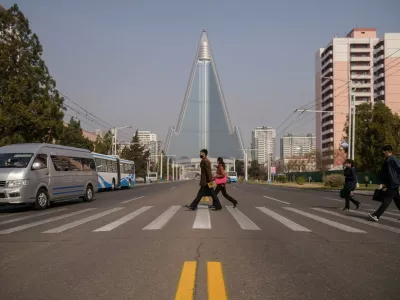 People wearing face masks walk across a street before the Ryugyong hotel (back C) on the occasion of the 108th birthday of late North Korean leader Kim Il Sung, known as the 'Day of the Sun', in Pyongyang on April 15, 2020.,Image: 513917283, License: Rights-managed, Restrictions:, Model Release: no